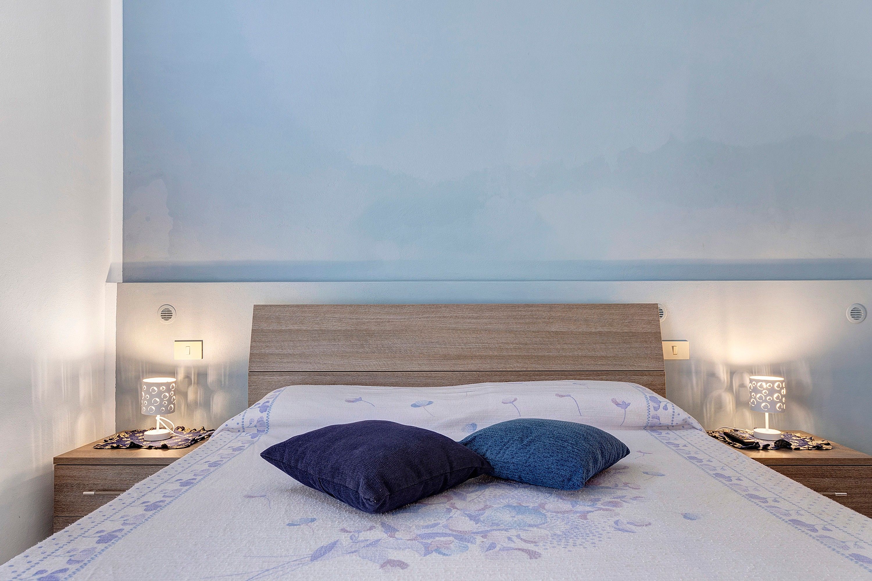 Een bed met een houten hoofdeinde, twee kussens en twee bedlampjes.