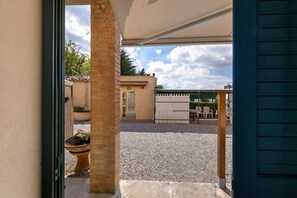 A covered outdoor patio with a gravel floor, a brick pillar, and a view of a building with a tiled roof. - Room 'Agriturismo Case Nuove - Camera Ste' with Shared Pool, Wi-Fi and Air Conditioning (Castellina Marittima)