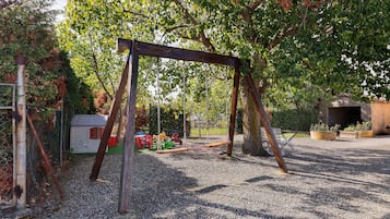 Un'area giochi con altalene, un piccolo deposito e fondo in ghiaia.