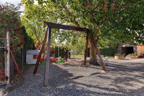 A playground with a swing set, a small shed, and a gravel surface.