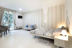 A bedroom with a bed, bedside table, lamp, and a desk with a chair. - Charming Studio Apartment With Ocean View in Riccione (Riccione)