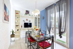 A modern living room with a glass dining table, red cushioned chairs, a flat-screen TV, and a large window with curtains. - Charming Modern Loft With Sea View in Riccione Hills (Riccione)