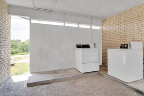 A laundry room with two white washing machines, a brick wall, and a concrete floor.