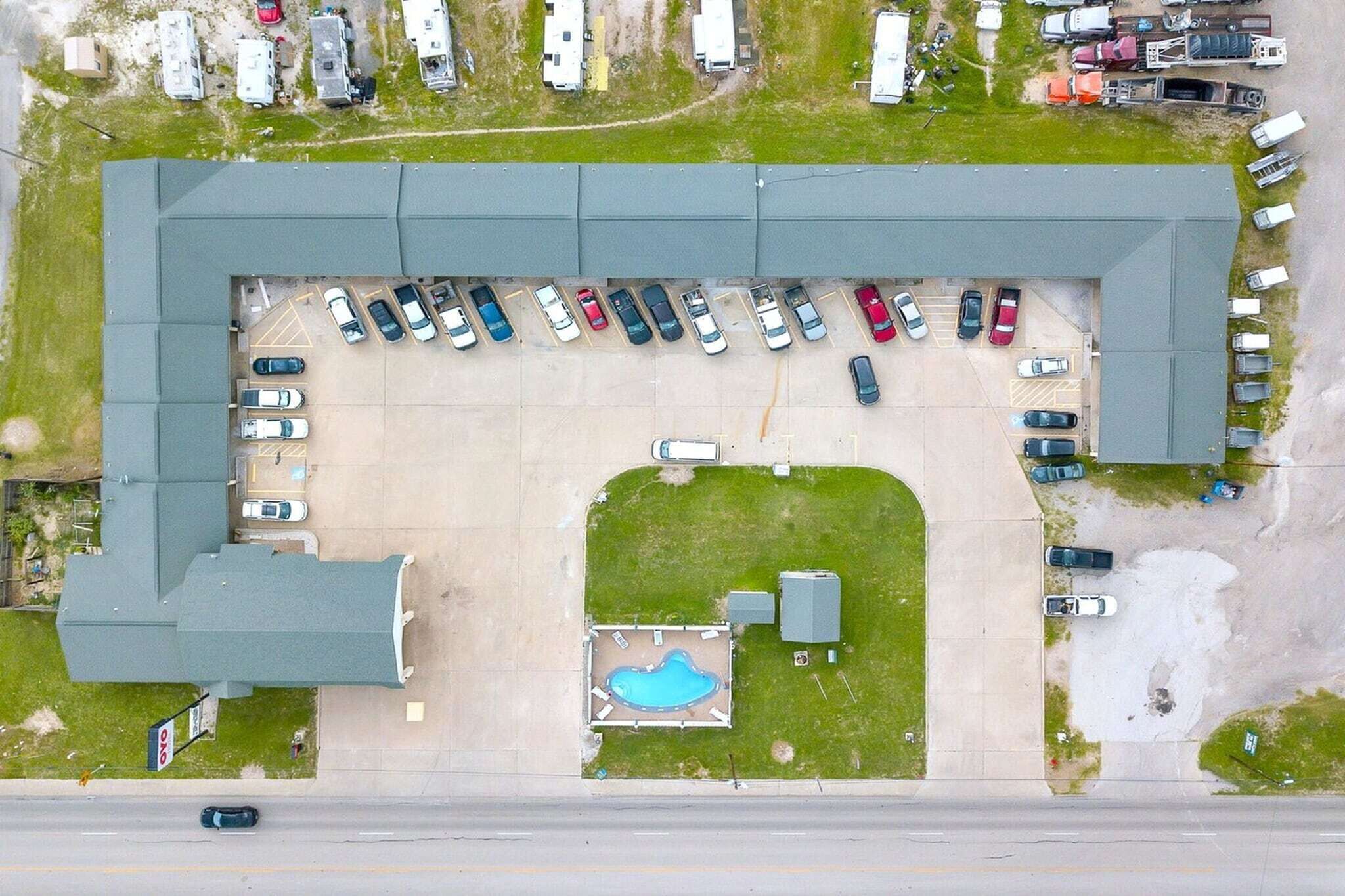 Vista aérea de un estacionamiento con varios coches, una piscina y un edificio con techo verde.