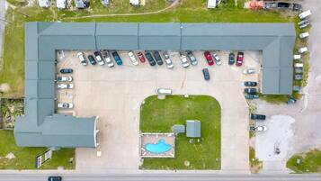 Vista aérea de un estacionamiento con varios coches, una piscina y un edificio con techo verde.