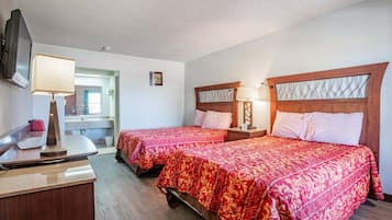 A hotel room with two beds, a desk with a lamp, and a bathroom visible through an open door.