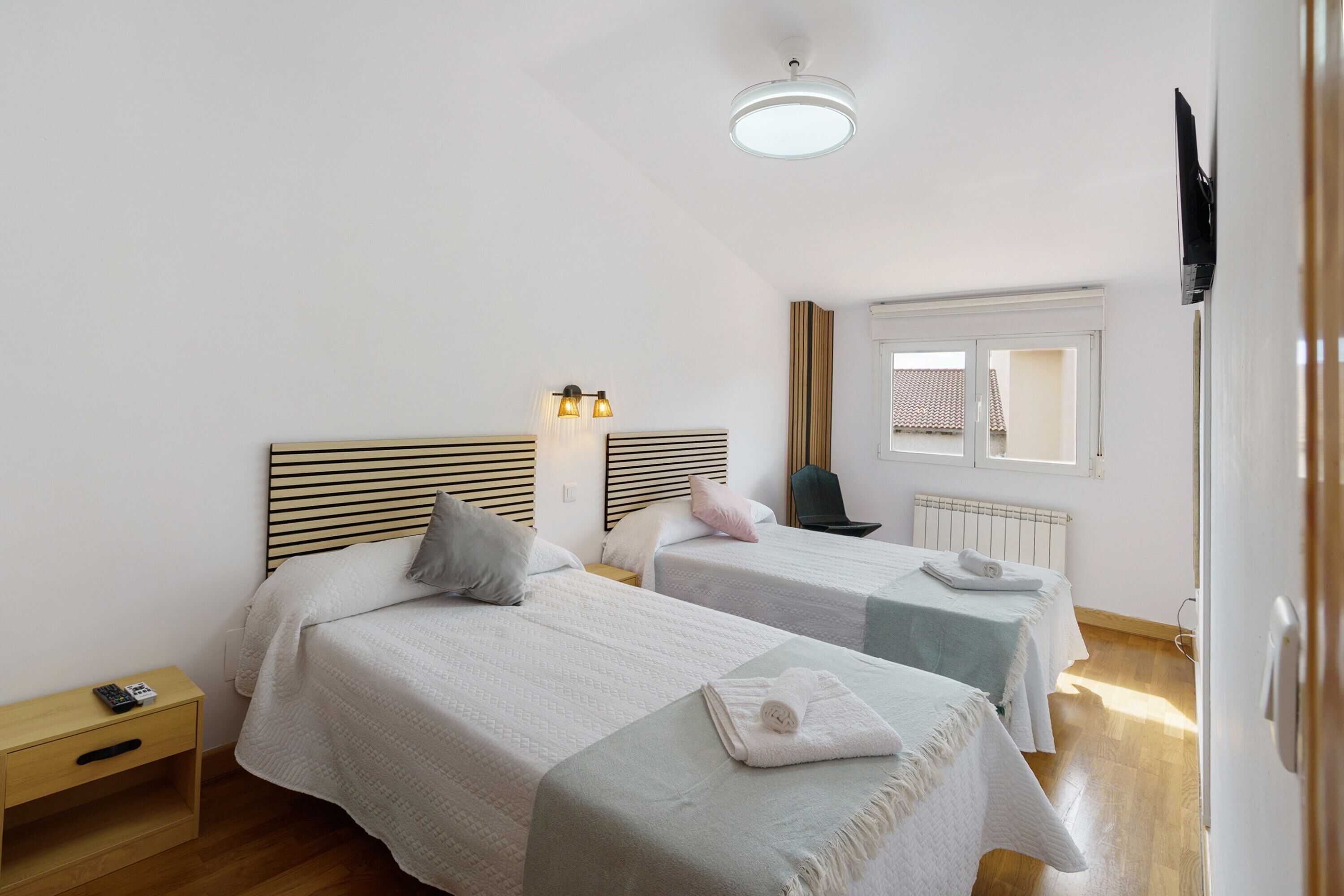 A hotel room with two beds, a nightstand, a chair, a window with a view, and a ceiling light fixture.