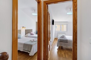 Un pasillo estrecho que conduce a un dormitorio con dos camas, un televisor y una ventana.