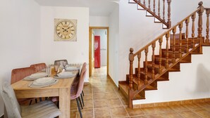 Een eetruimte met een houten tafel gedekt voor vier personen, een vintage klok en een trap met houten spijlen.