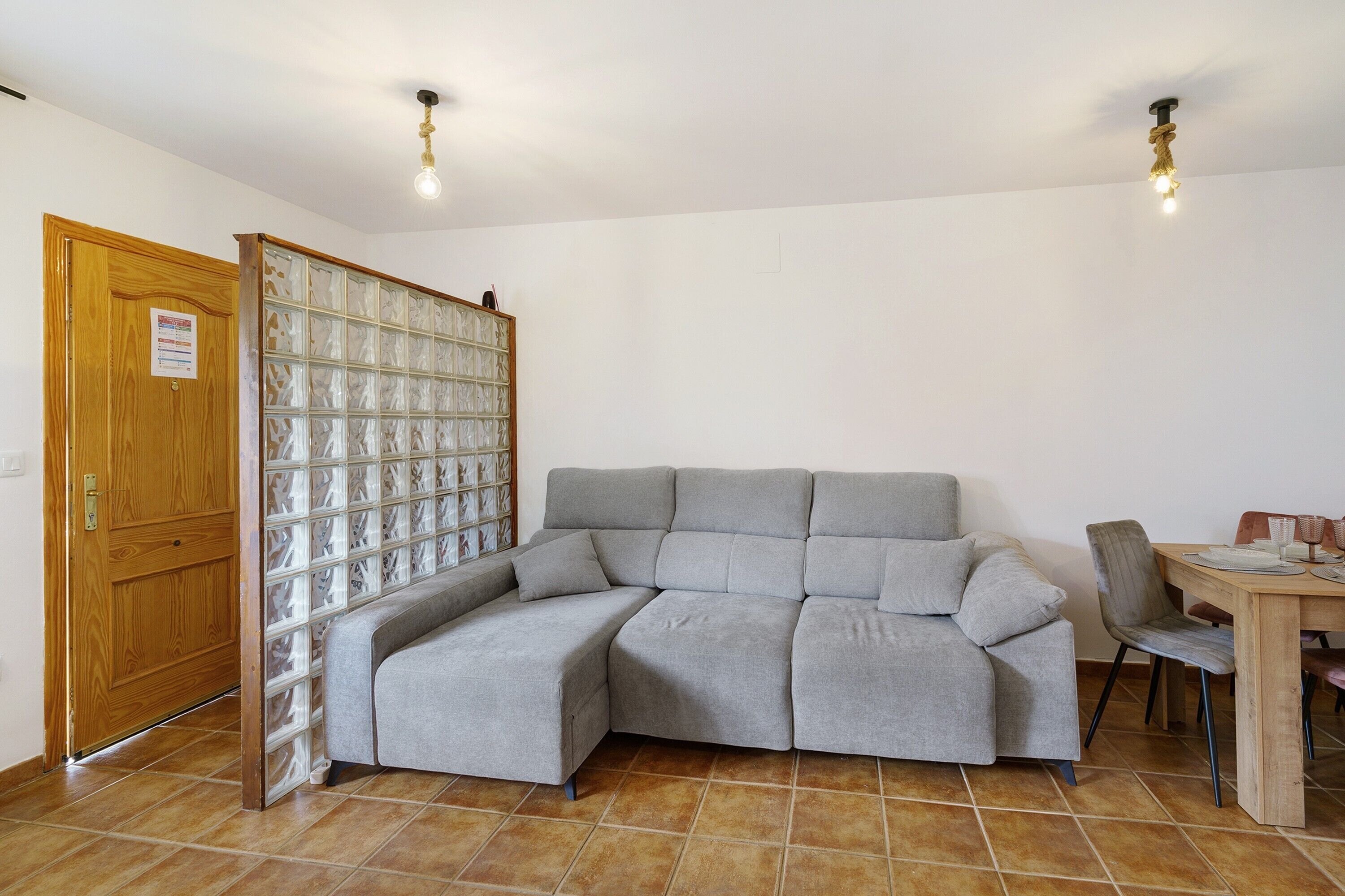 A room with a grey sectional sofa, a wooden door, a glass partition, and a dining table with chairs.