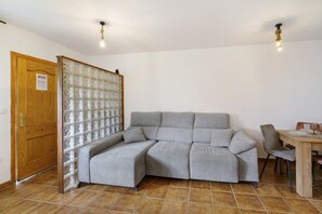 Et værelse med en grå hjørnesofa, en trædør, en glasvæg og et spisebord med stole.