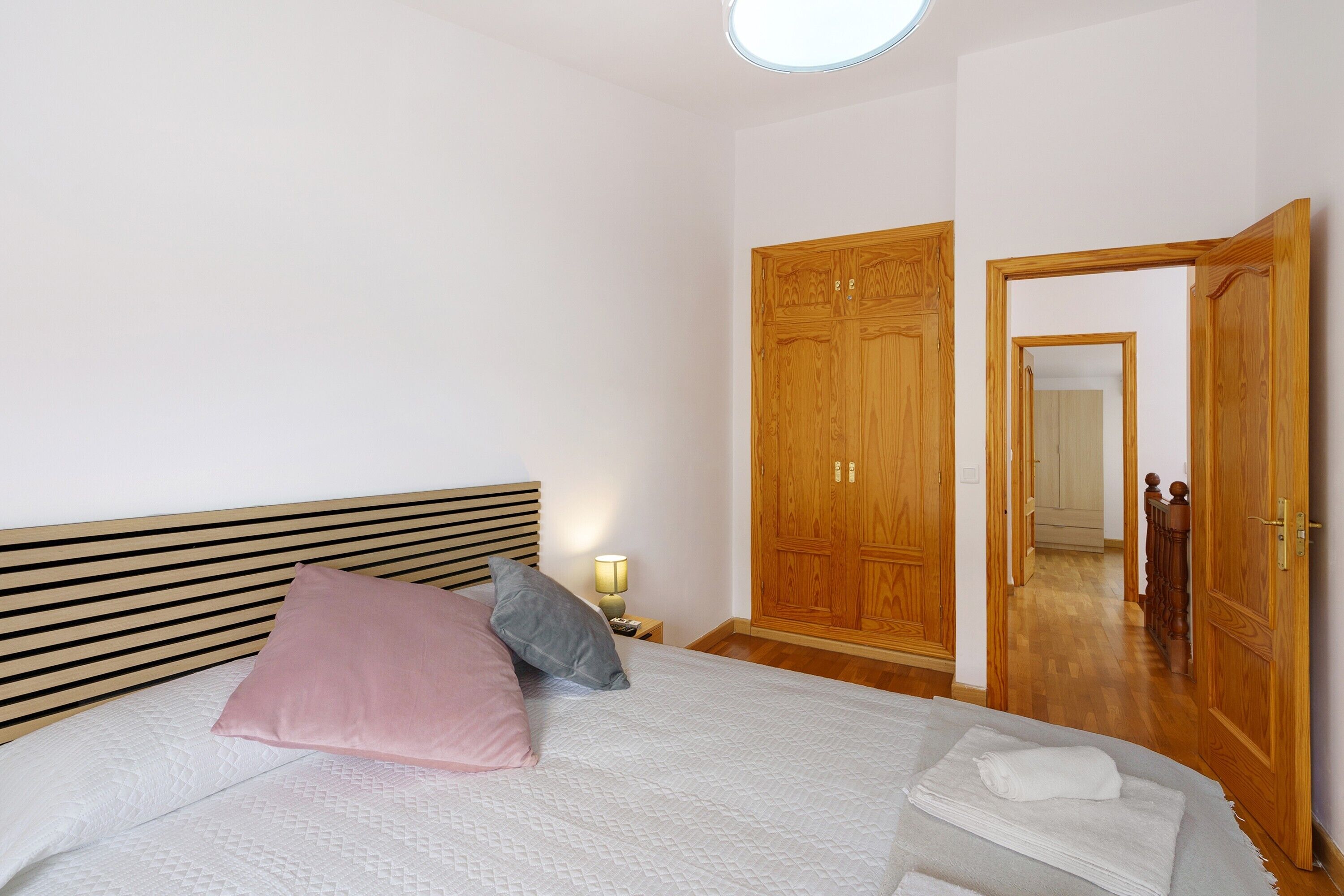 A bedroom with a bed, pillows, a bedside lamp, a wardrobe, and a mirror.