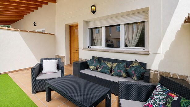 Een overdekt terras met rieten meubels, een houten deur en een raam met gordijnen.