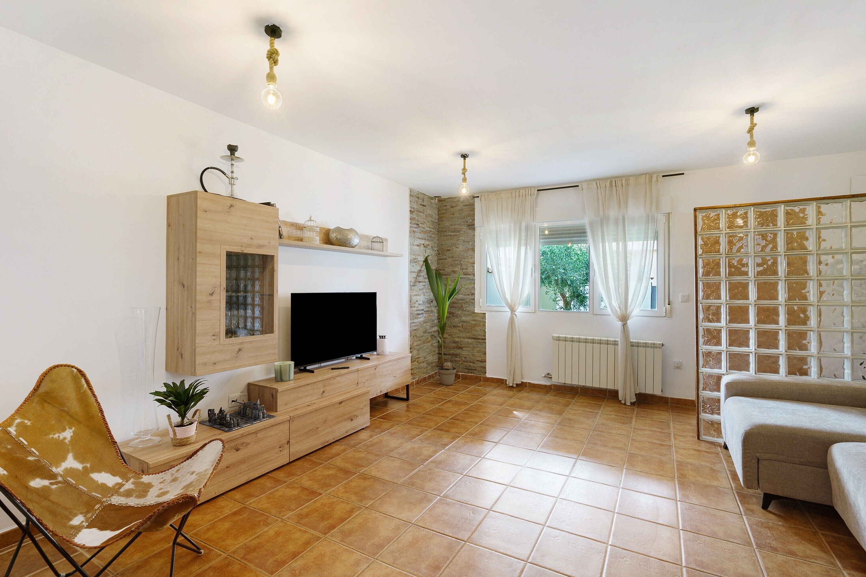 Una sala de estar con una televisión de pantalla plana, un mueble de madera para entretenimiento, un sofá, una silla y una planta en maceta.