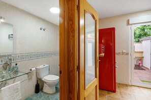 Un baño con inodoro, lavamanos de vidrio y una puerta roja que da a un espacio exterior.
