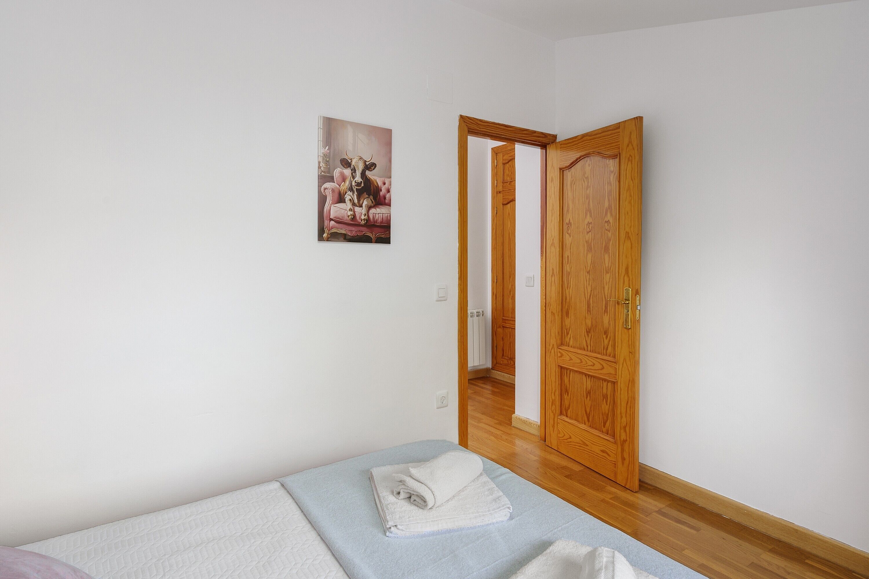 Un dormitorio con cama, una puerta y un cuadro colgado en la pared.