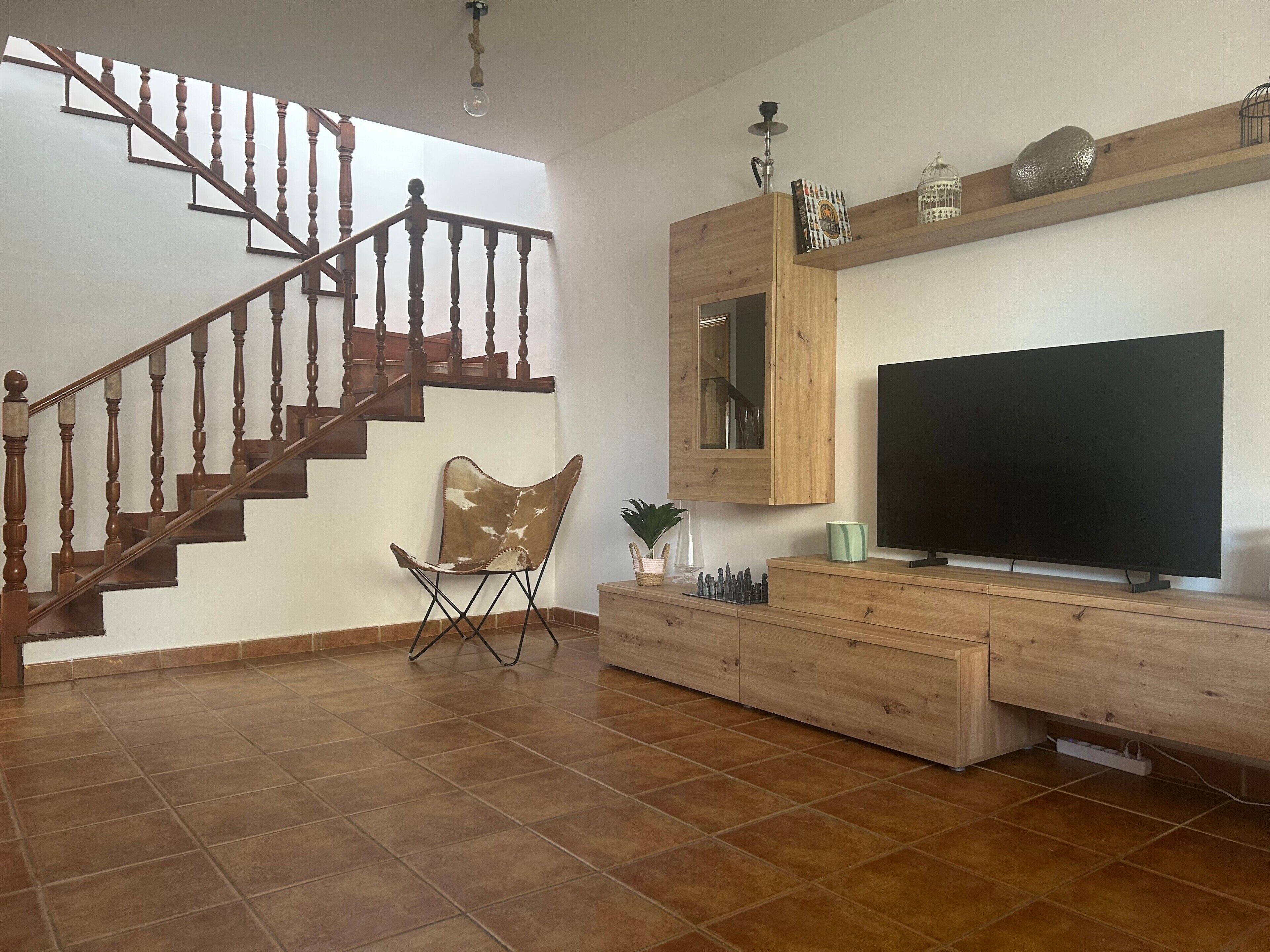 Een woonkamer met een houten trap, een flatscreen televisie, een houten entertainmentkast en een stoel.