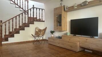 Een woonkamer met een houten trap, een flatscreen televisie, een houten entertainmentkast en een stoel.