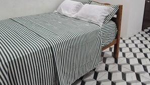 A single bed with a striped bedspread and pillows, a white wall with an air conditioning unit, and a checkered floor pattern.