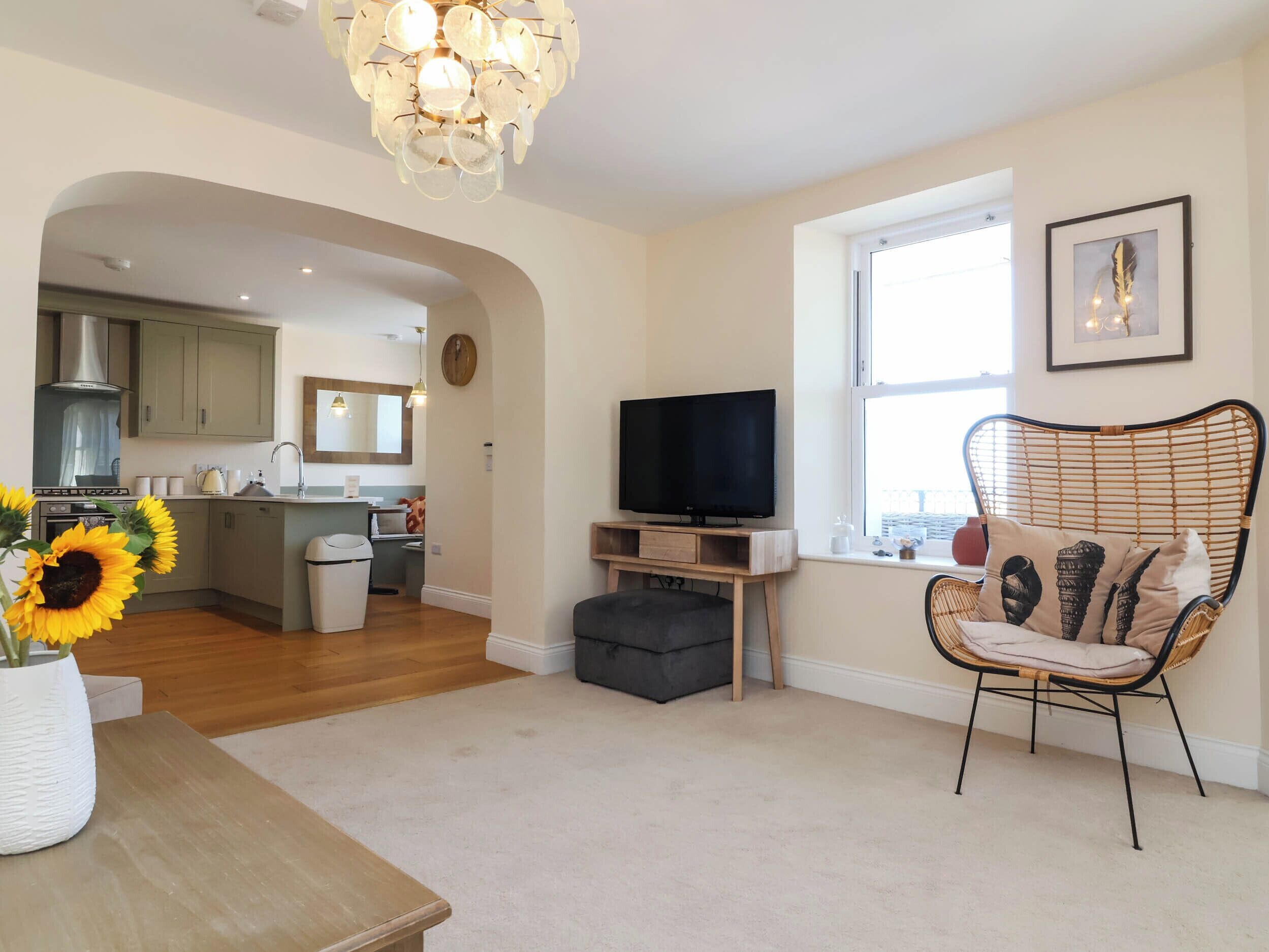 A modern living room with a television, a wicker chair, and a kitchen in the background.