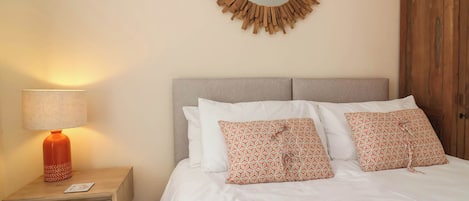 A bedroom with a bed, a nightstand with a lamp, a mirror, and a wardrobe.