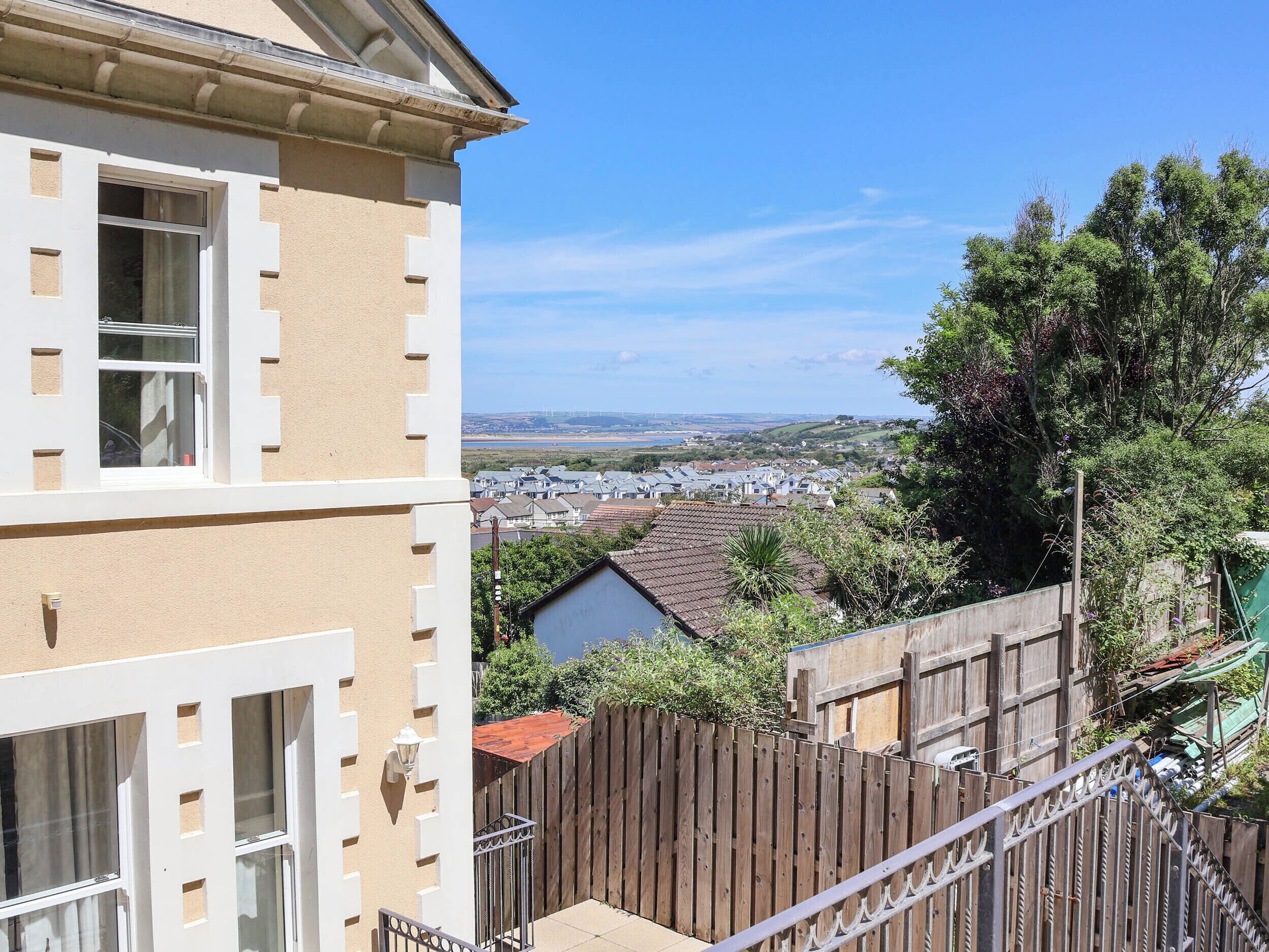 A residential building with a balcony, a wooden fence, and a view of a town and landscape.
