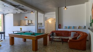 Ein Zimmer mit Billardtisch, einer Couch, einem kleinen Tisch mit Vase und einem an der Wand befestigten Feuerlöscher.