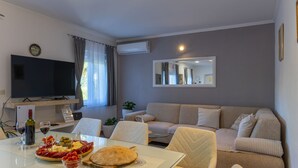 Ein Wohnzimmer mit Fernseher, Sofa, Esstisch mit Speisen und einem Spiegel.