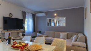 A living room with a TV, sofa, dining table with food, and a mirror. - Villa Emanuela by Villas Guide (Grubine)