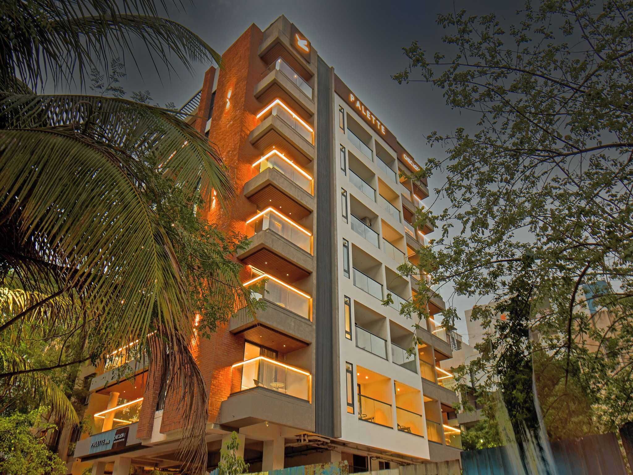 Un hotel de varios pisos con balcones, una estructura vertical central y vegetación circundante.