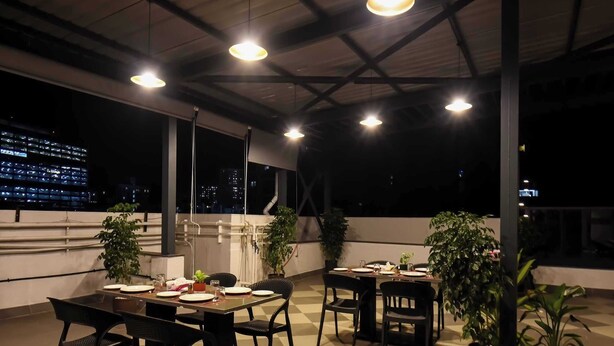 An outdoor dining area with tables and chairs, potted plants, and a view of the cityscape at night. - Palette Hotel and Residences Baner Pune (Pune)