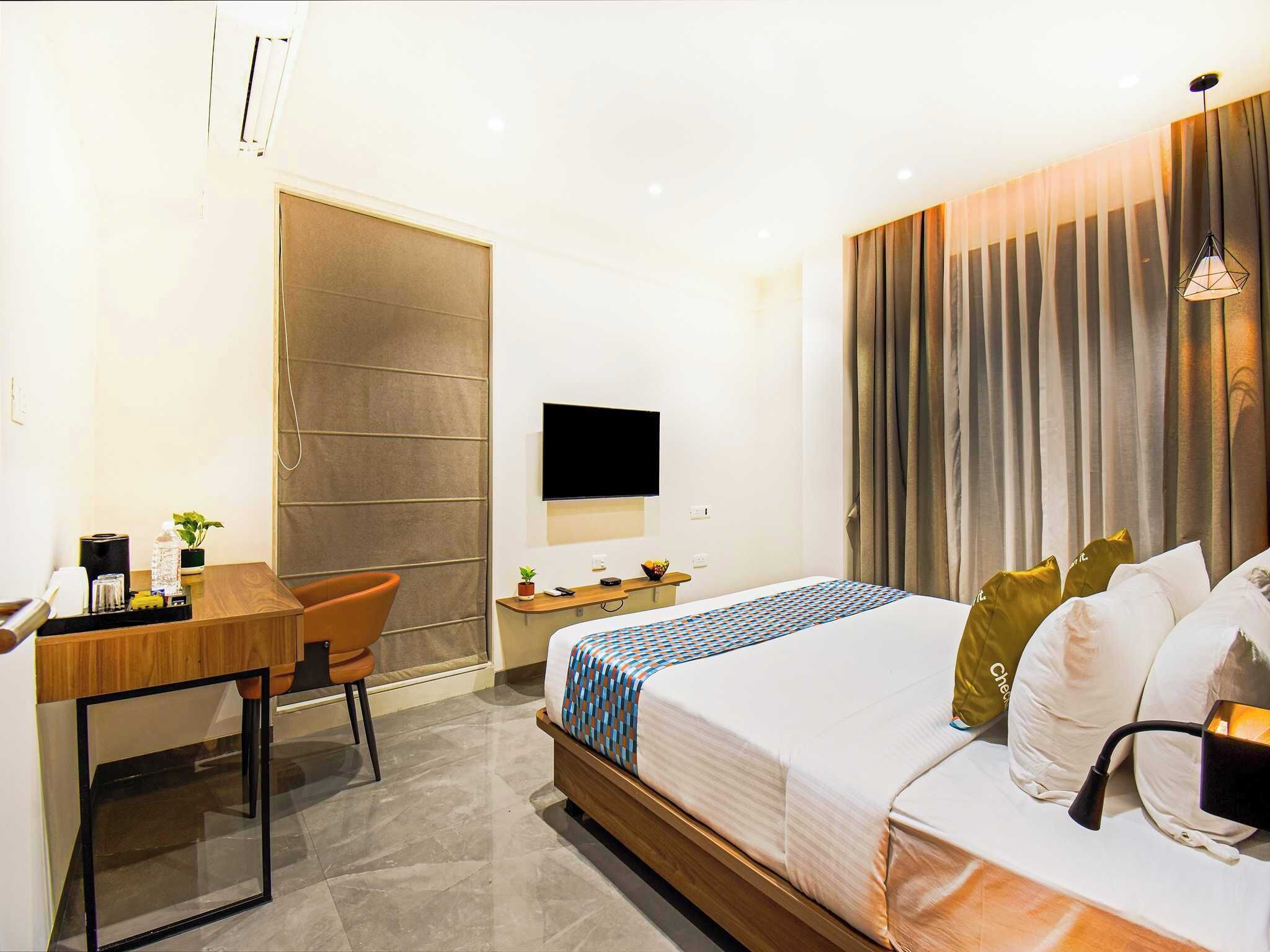 A hotel room with a bed, a desk, a chair, a TV, and a window with curtains.
