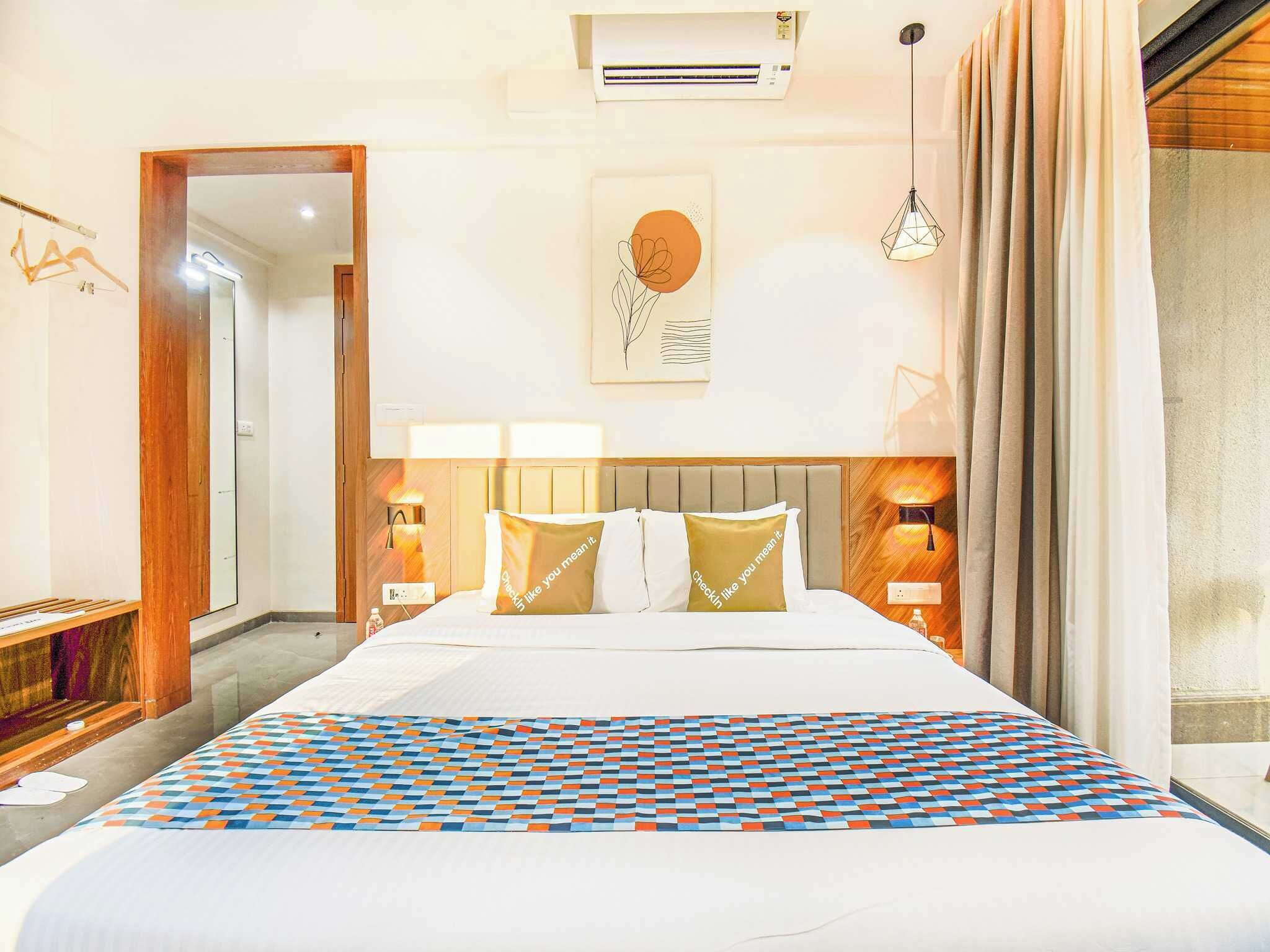 Habitación de hotel con una cama grande, dos lámparas de noche, aire acondicionado montado en la pared y una ventana con cortinas.