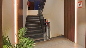 A staircase with a metal railing, a fire exit sign, and a potted plant. - Palette Hotel and Residences Baner Pune (Pune)