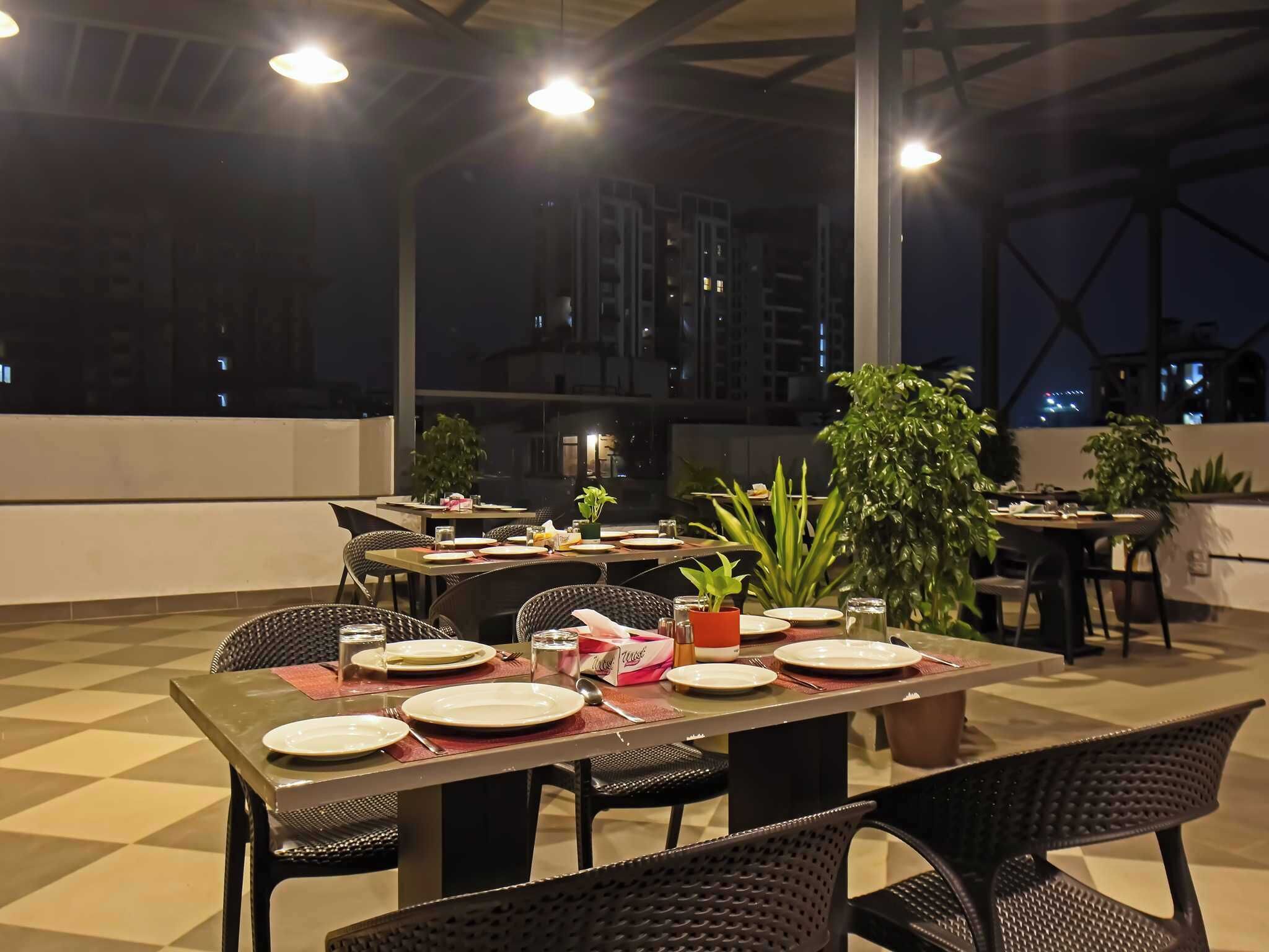 Un espace extérieur aménagé pour les repas, avec des tables pour deux personnes, entourées de chaises et agrémenté de plantes en pot.