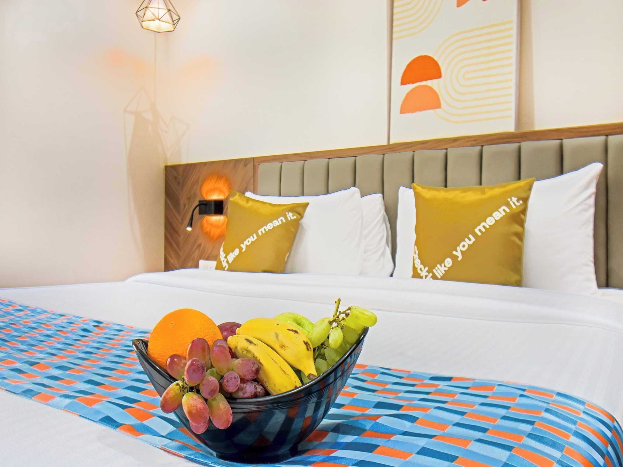 A hotel room with a bed, a bowl of fruit, and a patterned bedspread.