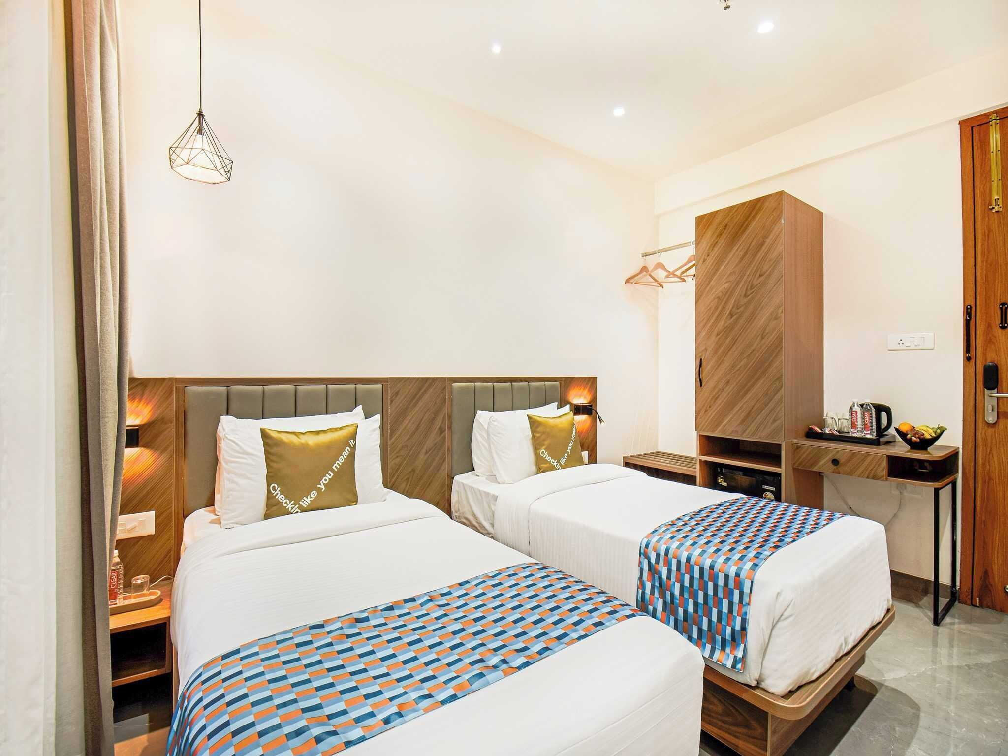A hotel room with two beds, a wardrobe, a desk, and a hanging light fixture.