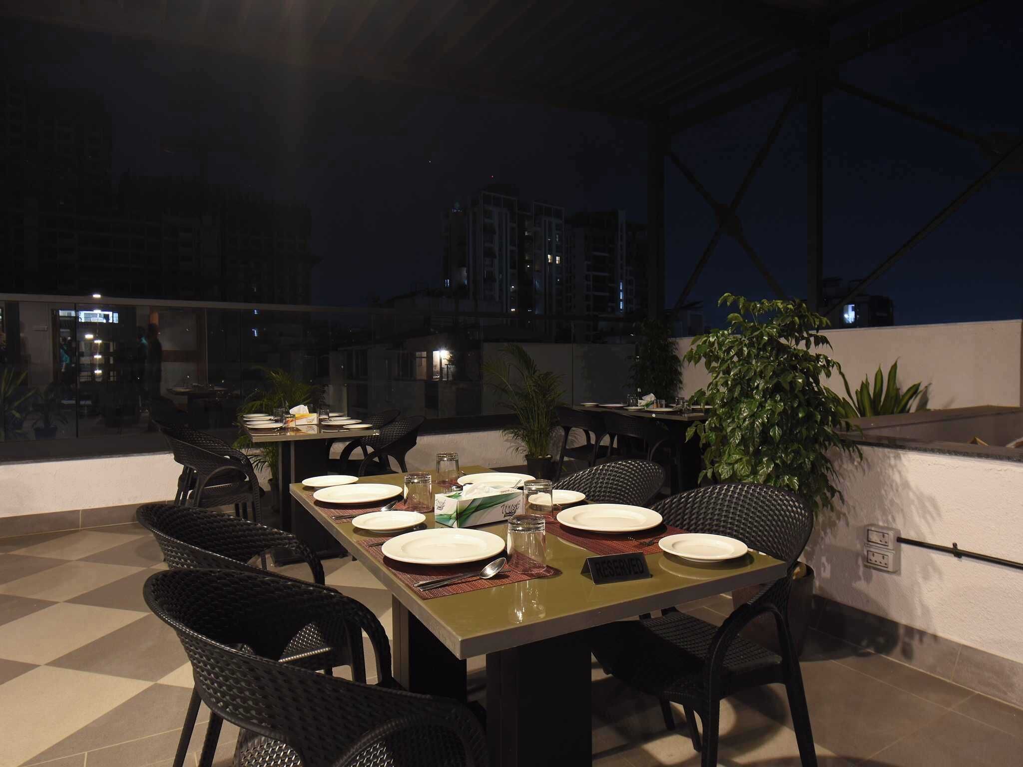 An outdoor dining area with tables set for four, surrounded by wicker chairs, and a view of buildings in the background.