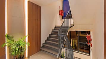A modern staircase with a metal railing, a potted plant, and a fire extinguisher on the wall.