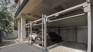 A covered parking garage with a car on a lift, a gated entrance, and a building with a concrete facade. - Palette Hotel and Residences Baner Pune (Pune)