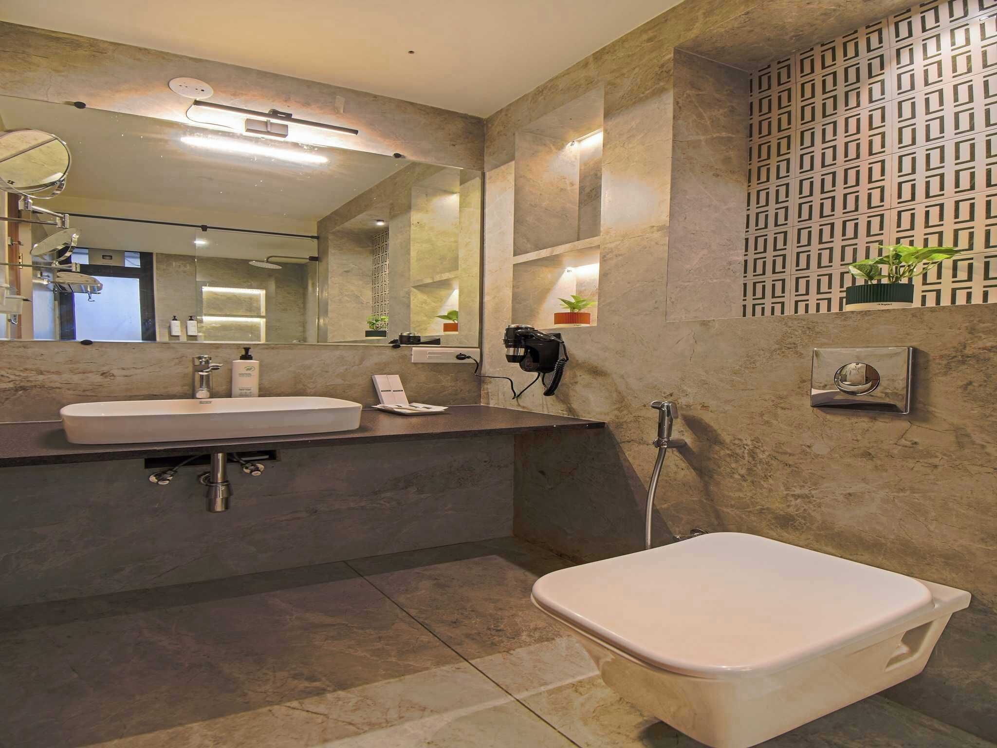 Une salle de bain moderne avec un grand miroir, deux vasques, des toilettes et une douche.