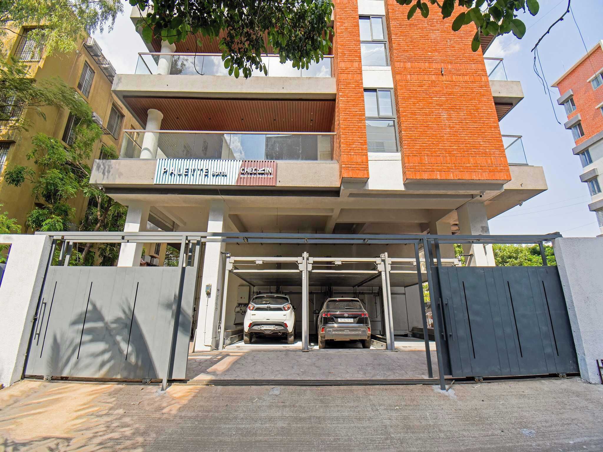 Edificio de varios pisos con entrada porticada, dos coches estacionados en el interior y un balcón visible con un letrero.