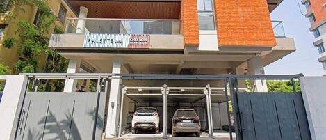 A multi-story building with a gated entrance, two cars parked inside, and a visible balcony with a sign.