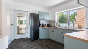 A modern kitchen with a black refrigerator, light blue cabinets, and a large window offering a view of the outdoors. - Panoramic Lake House at Steinhuder Meer – Your Exclusive Retreat by the Water (Wunstorf)