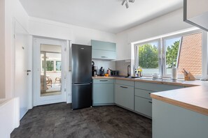 Eine moderne Küche mit einem schwarzen Kühlschrank, hellblauen Schränken und einem großen Fenster mit Blick ins Freie.