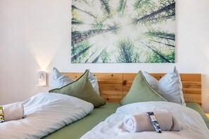 Ein ordentlich bezogenes Bett mit Kissen, einem hölzernen Kopfteil und einem an der Wand hängenden Bild von einem Wald.