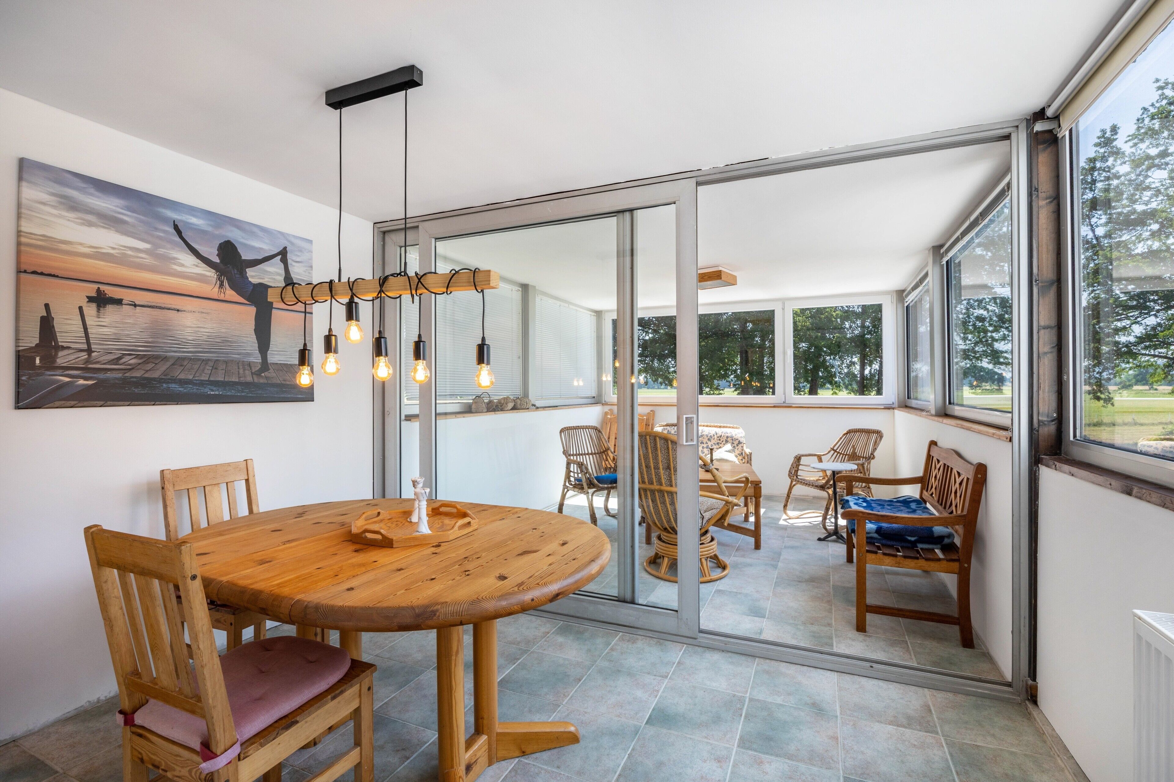 A dining area with a wooden table and chairs, a pendant light, and a large window with a view of the outdoors.