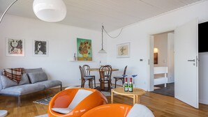 A modern living room with a sofa, orange chairs, a dining table, and artwork on the walls. - Panoramic Lake House at Steinhuder Meer – Your Exclusive Retreat by the Water (Wunstorf)
