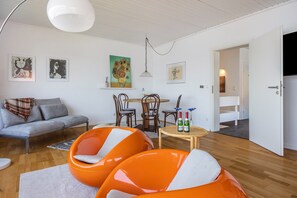 Ein modernes Wohnzimmer mit einer Couch, orangefarbenen Sesseln, einem Esstisch und Kunstwerken an den Wänden.