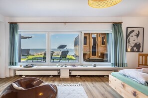 A room with a large window overlooking a body of water, a bed, a chair, and a small table with items on it. - Panoramic Lake House at Steinhuder Meer – Your Exclusive Retreat by the Water (Wunstorf)